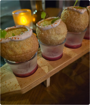 Three pani puri shots on wooden board